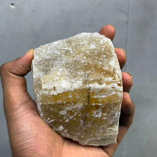 Natural honey calcite rough gemstone chunk held in hand