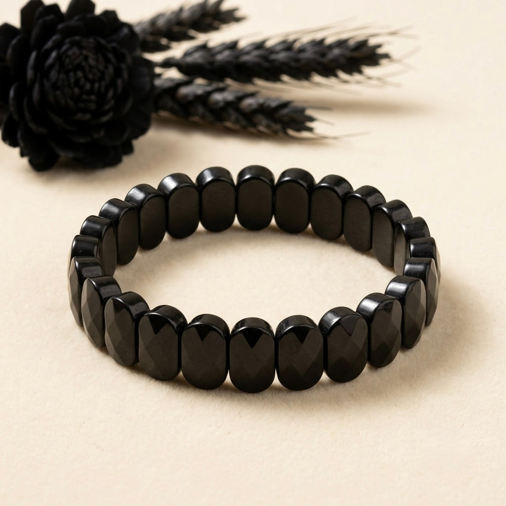 Natural onyx bracelet oval faceted black beads on light background with tassel accessory