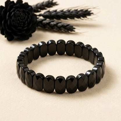 Natural onyx bracelet oval faceted black beads on light background with tassel accessory