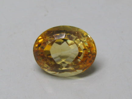 Oval natural citrine gemstone with warm yellow-brown tones on a light background