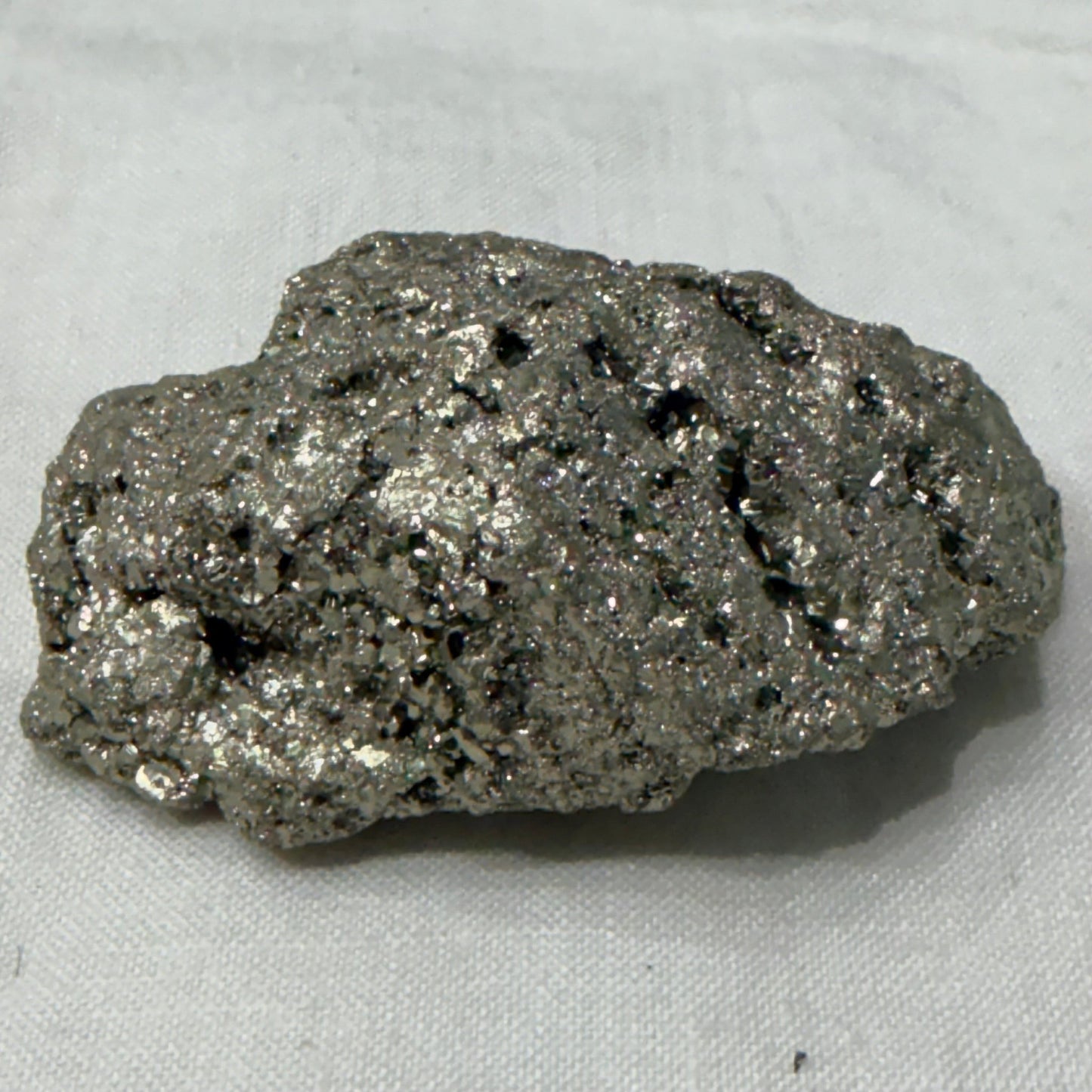 Natural raw pyrite crystal specimen with metallic brassy glitter on light fabric