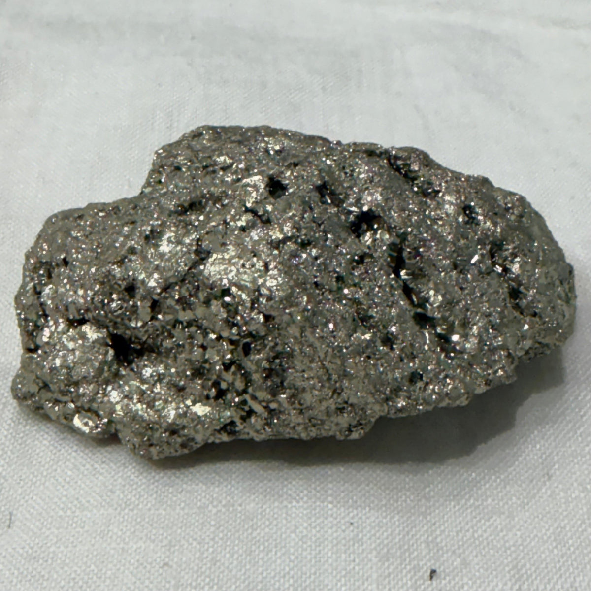 Natural raw pyrite crystal specimen with metallic brassy glitter on light fabric