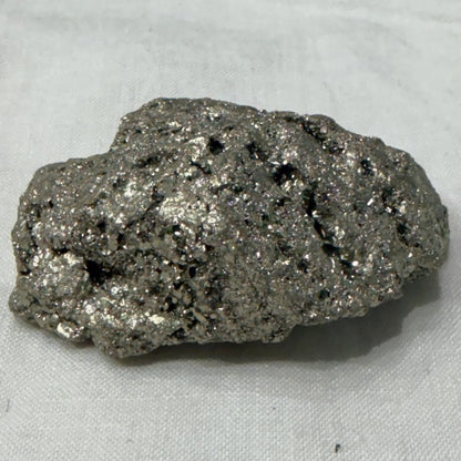Natural raw pyrite crystal specimen with metallic brassy glitter on light fabric