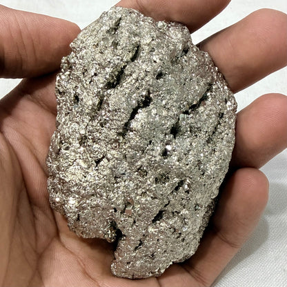 Natural raw pyrite crystal held in hands, showing rough metallic surface texture