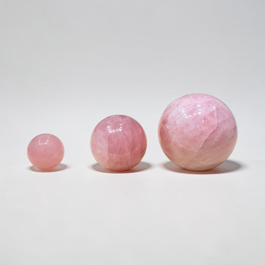 Natural rose quartz crystal ball spheres in soft pink, studio close-up on white background