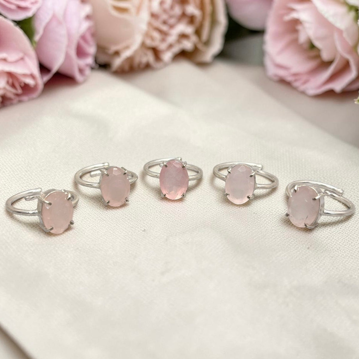 Natural rose quartz adjustable ring featuring a pink oval stone on white fabric background