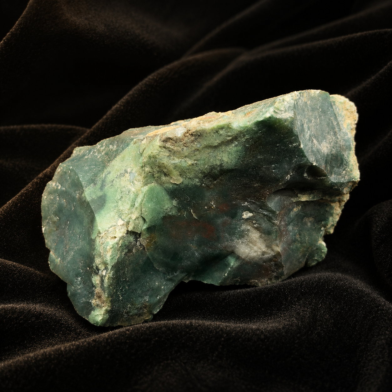 Natural rough bloodstone gemstone with green and dark speckled surface on black fabric