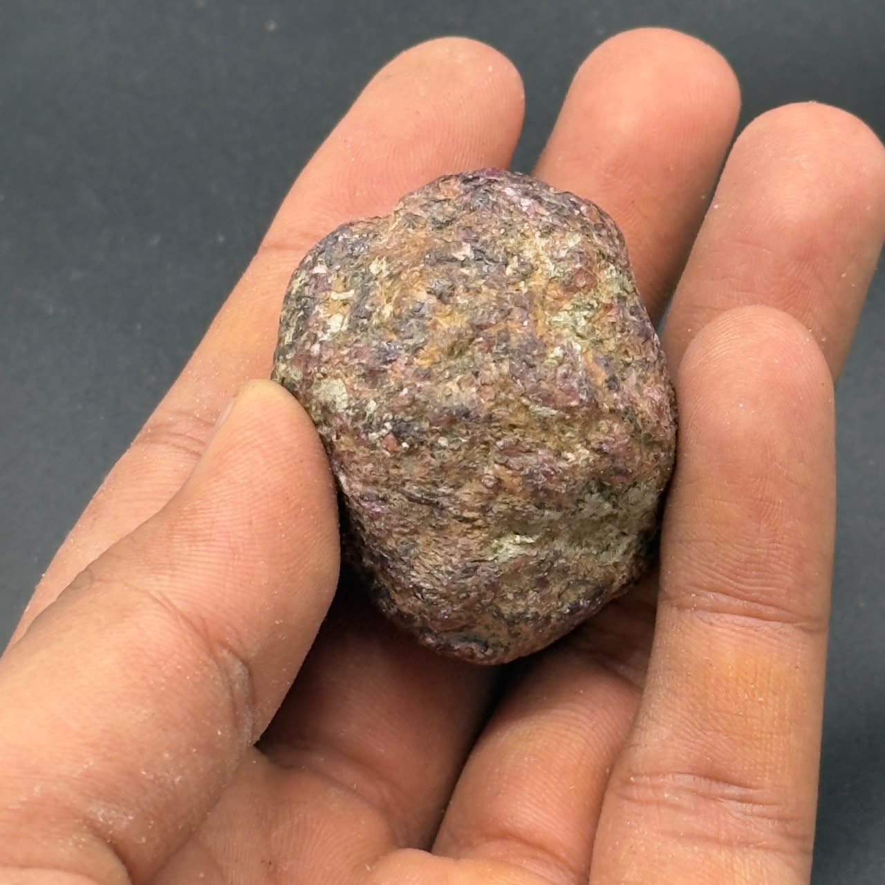 Natural rough hessonite garnet stone held in hand for size, textured multicolor surface