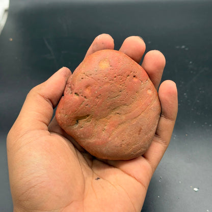 Natural rough red jasper stone held in hand, smooth pebble form with speckled texture