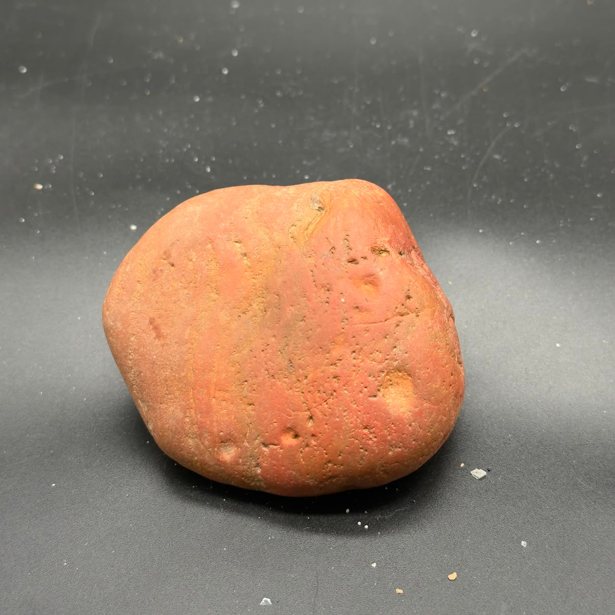 Natural rough red jasper stone, tumbled pebble shape on dark gray surface