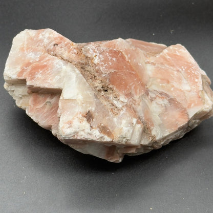Natural sunstone rough crystal with peach and white mineral texture on gray background