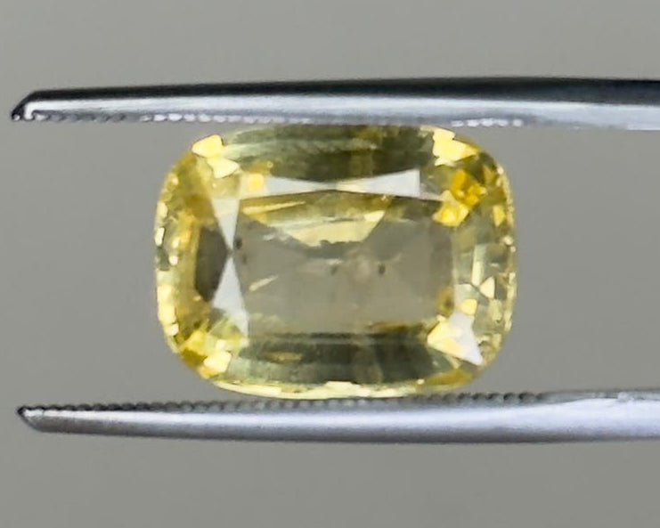 Natural yellow sapphire cushion cut gemstone on a metal display tweezers