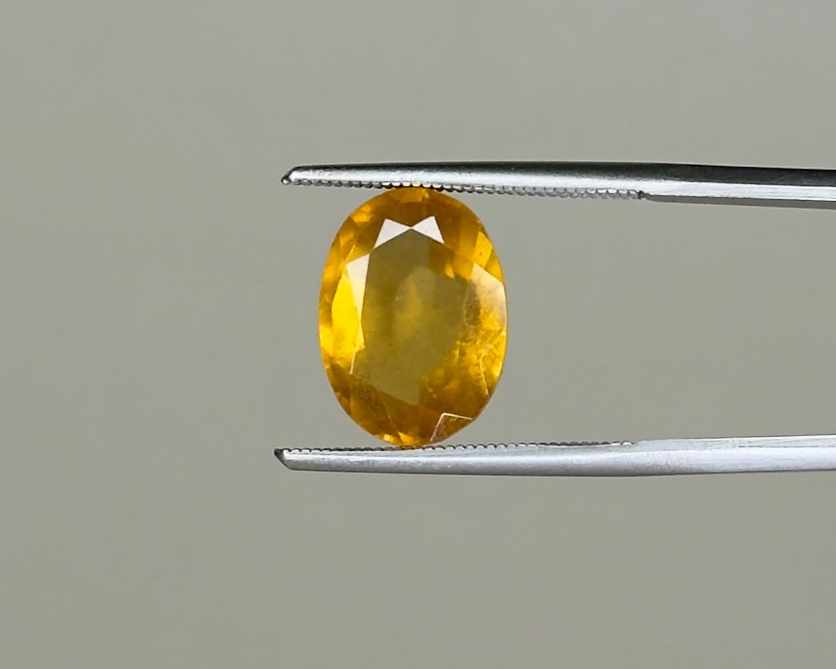 Oval cut natural hessonite garnet gemstone in metal tweezers, yellow-brown color