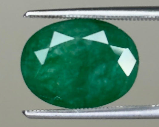 Oval emerald gemstone with bright green color held between metal tweezers