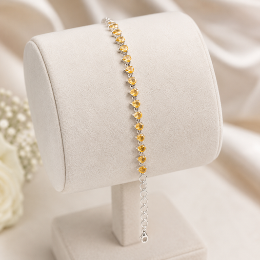 Pear-cut golden citrine sunela bracelet on beige jewelry stand with silver chain and lobster clasp