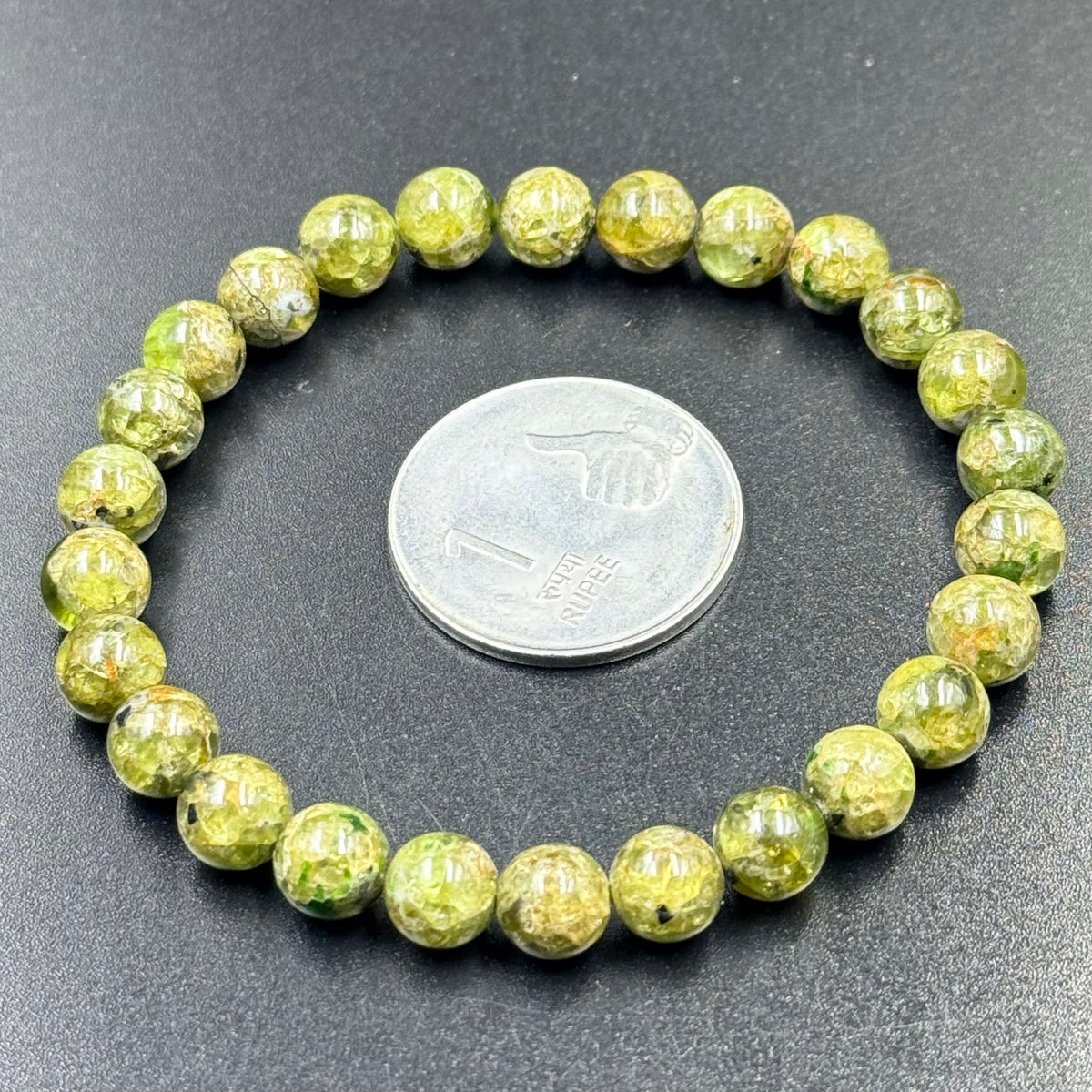 Peridot AA quality bracelet laid out beside a coin for size comparison