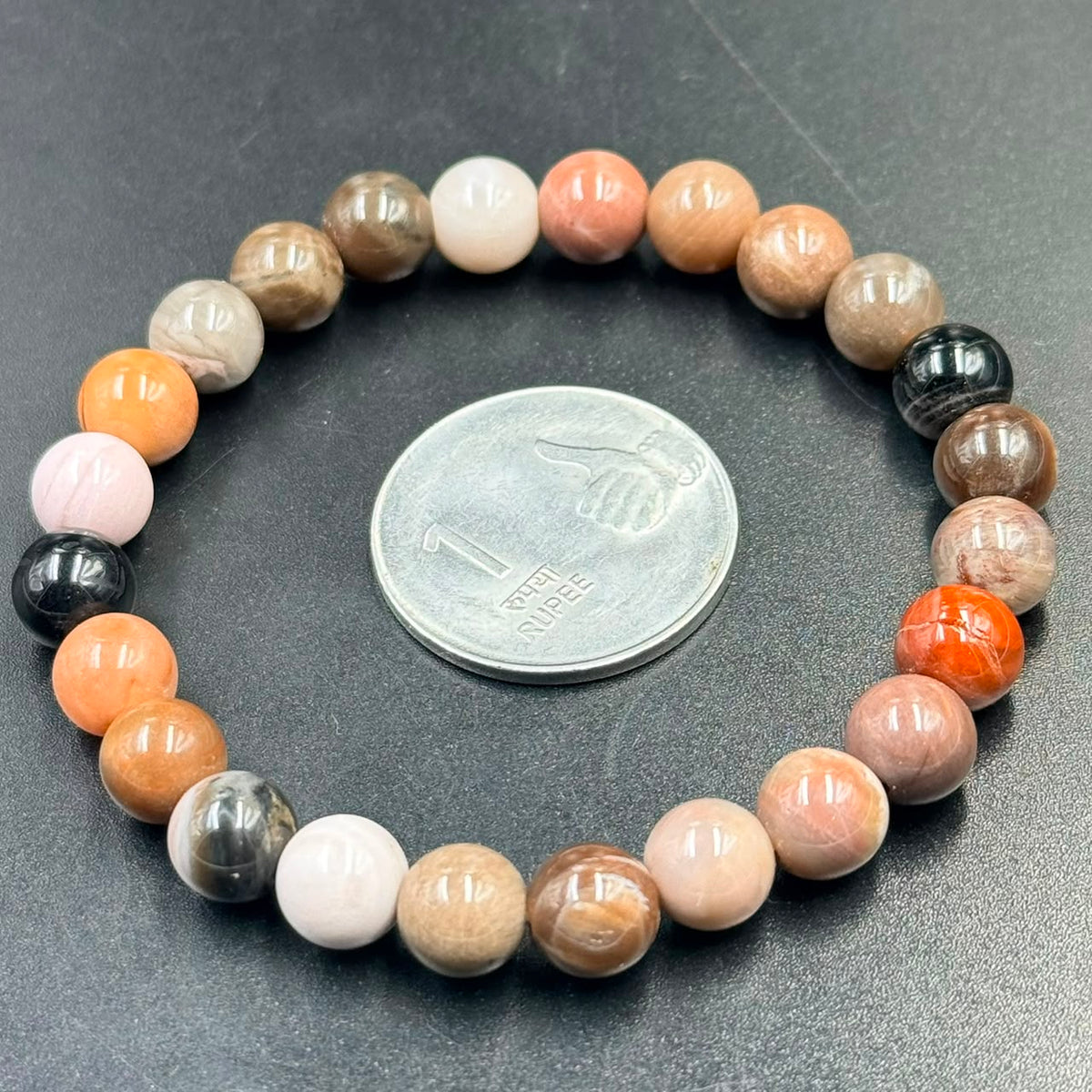Petrified wood bracelet with colorful beads on dark slate beside a coin for size