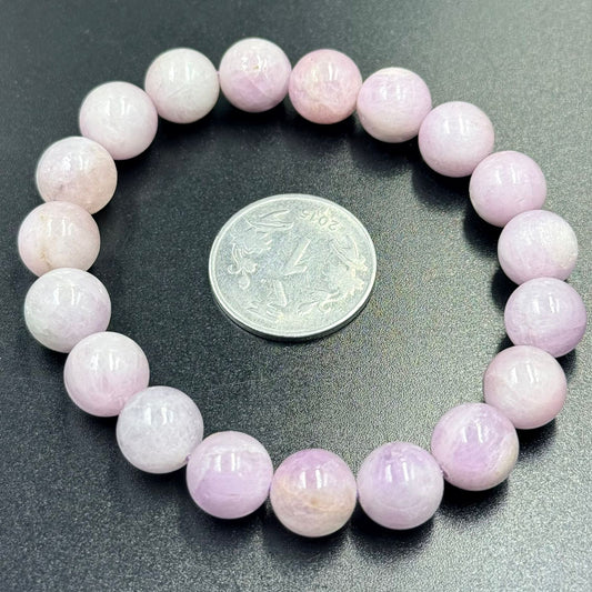 Pink kunzite bracelet with round beads shown around a coin for size reference