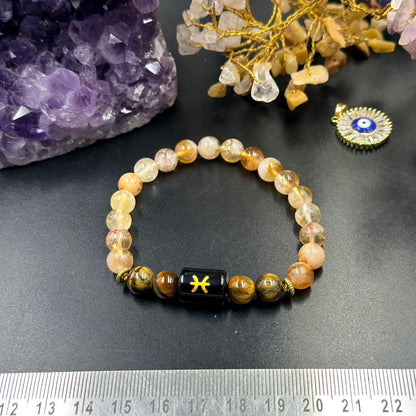 Pisces zodiac bracelet with citrine and tiger eye beads and black Pisces charm on dark surface