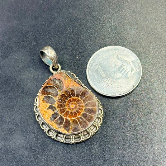 Polished ammonite fossil in 925 silver locket pendant with ornate bail on dark surface