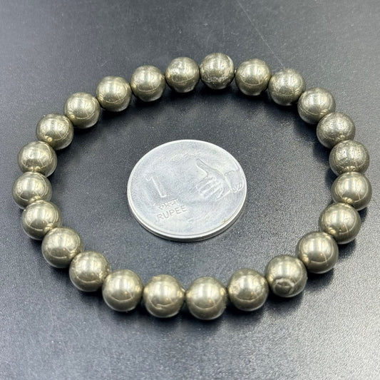 Pyrite bracelet with round metallic beads shown next to a coin on dark fabric