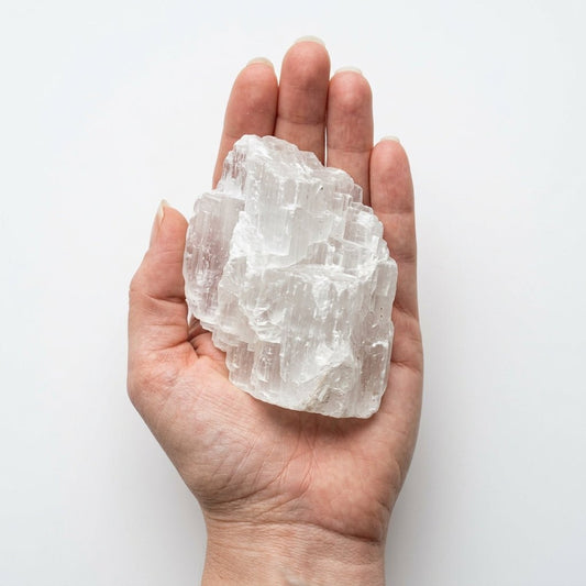 Raw white selenite crystal held in open hand for size comparison