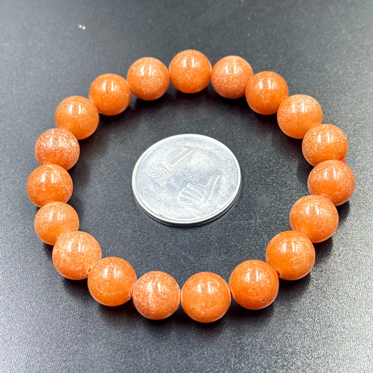 Red aventurine bead bracelet with round stones, close-up with coin for scale