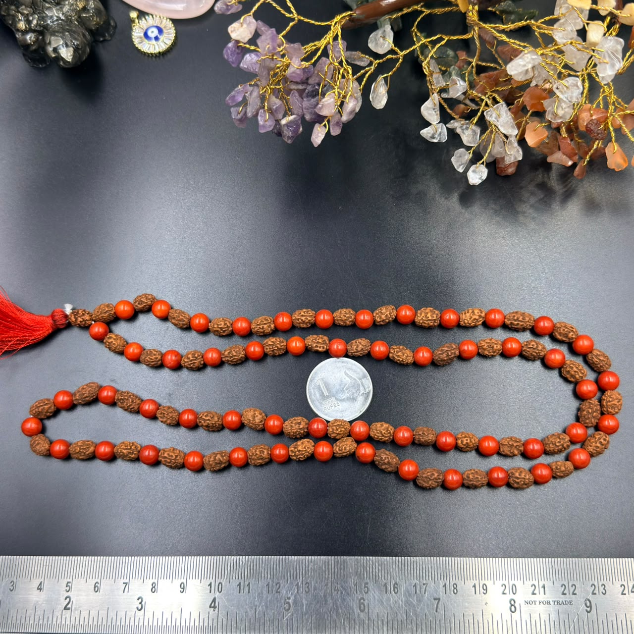 Red coral bead and rudraksha jap mala strands with red tassel shown on measuring board