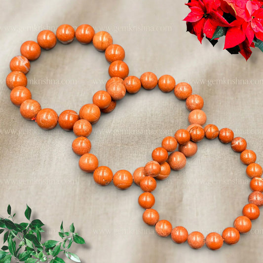 Red jasper bracelet made of smooth round beads arranged in a flat oval on gray fabric