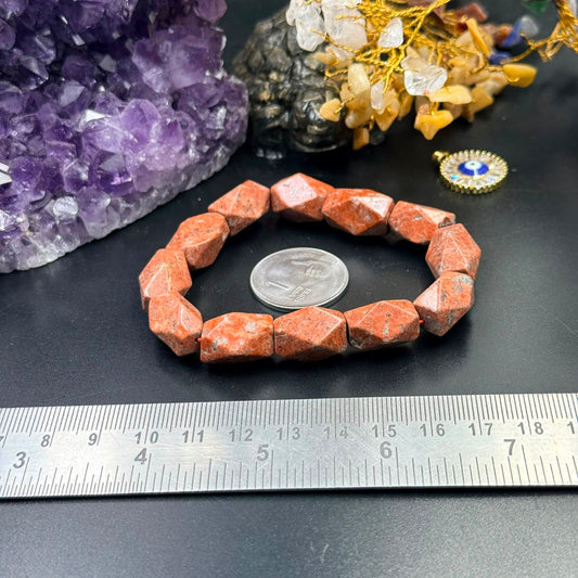 Red jasper faceted tumble bracelet with orange-red stones on black surface