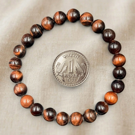 Red tiger eye bracelet with glowing striped bead pattern, flat lay with coin for scale