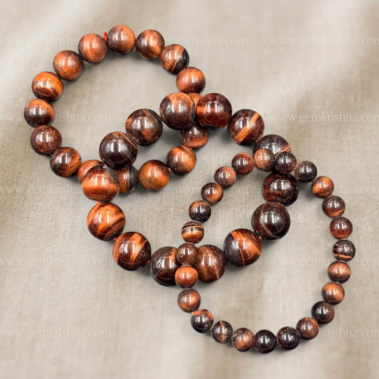 Red tiger eye bracelet shown with polished round beads arranged in a circle on fabric