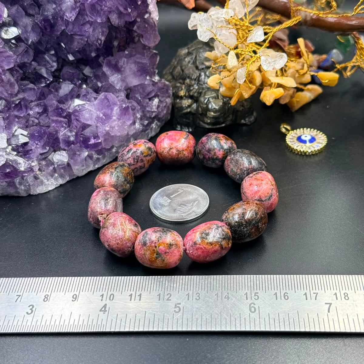 Rhodonite tumble bead bracelet with oval stones on dark surface beside amethyst and a ruler