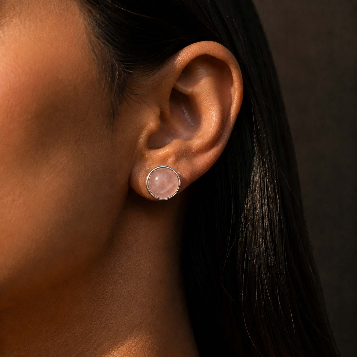 Natural rose quartz cabochon stud earrings in German silver worn on ear with long dark hair