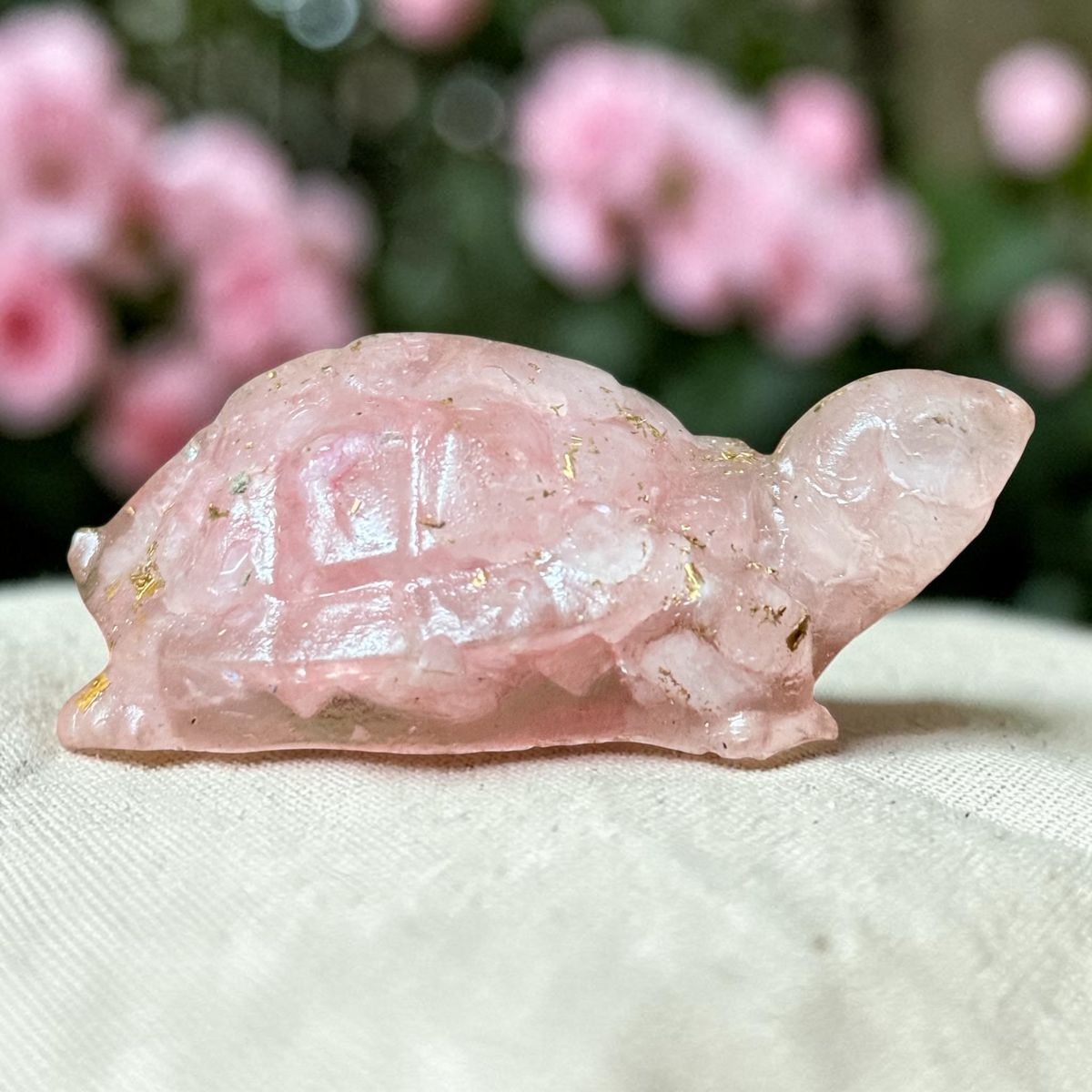Rose quartz turtle figurine with natural sparkly inclusions on a soft fabric