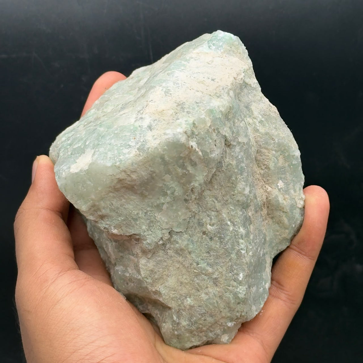 Rough Amazonite stone held in a hand, pale aqua and white natural texture