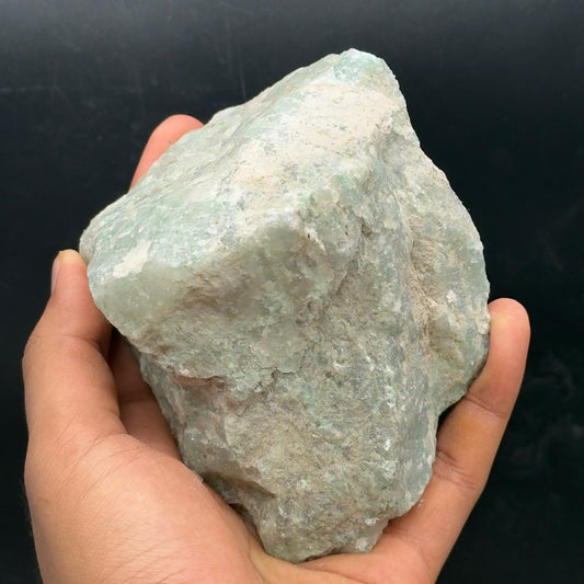 Rough Amazonite stone held in a hand, pale aqua and white natural texture