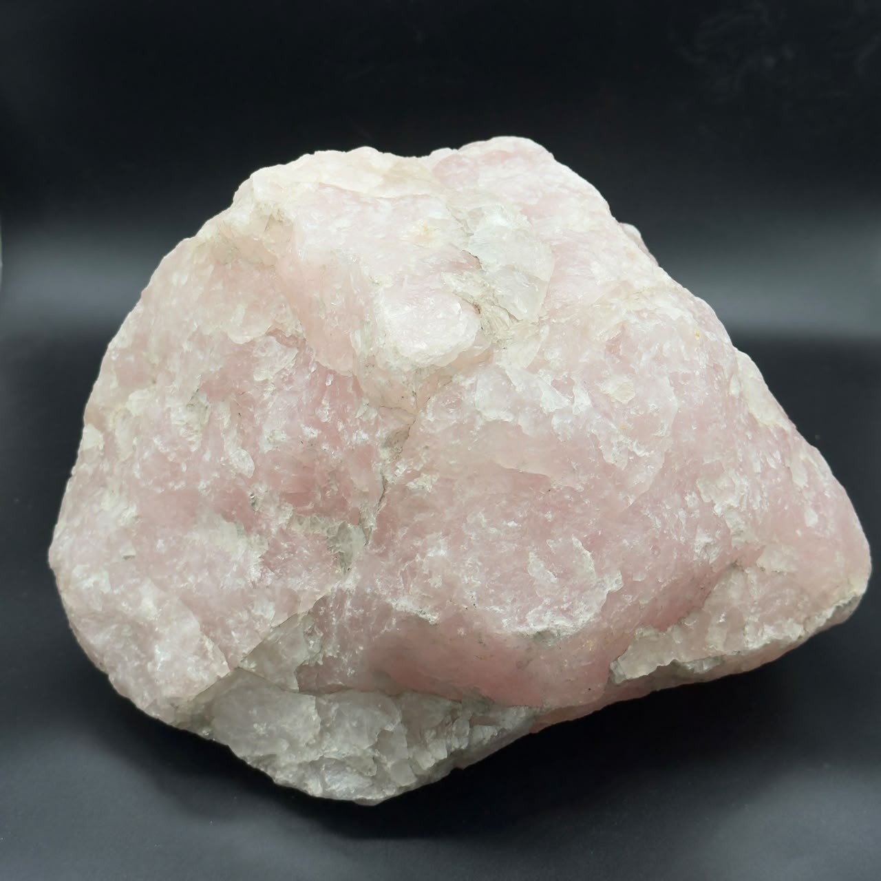 Close-up of rough rose quartz with pale pink and white crystal facets on dark background