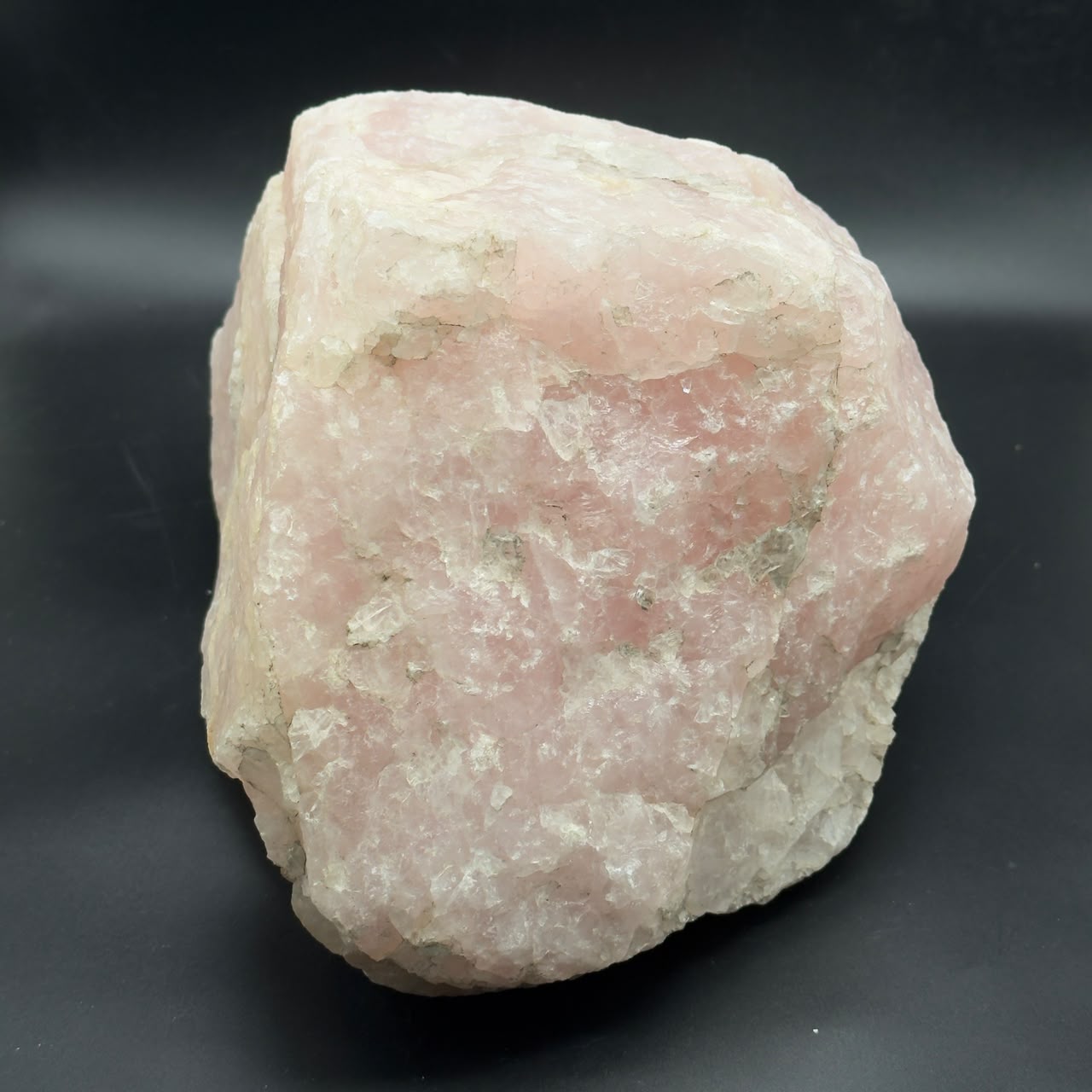 Rough rose quartz crystal with creamy white top and pale pink body on dark background