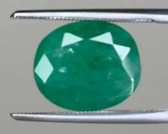 Round emerald green gemstone held between two metal tweezers