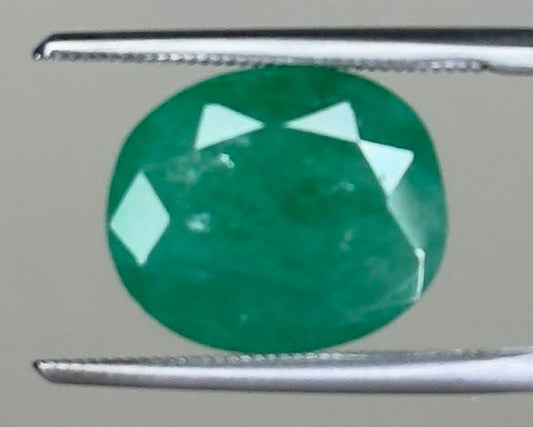 Round emerald green gemstone held between two metal tweezers
