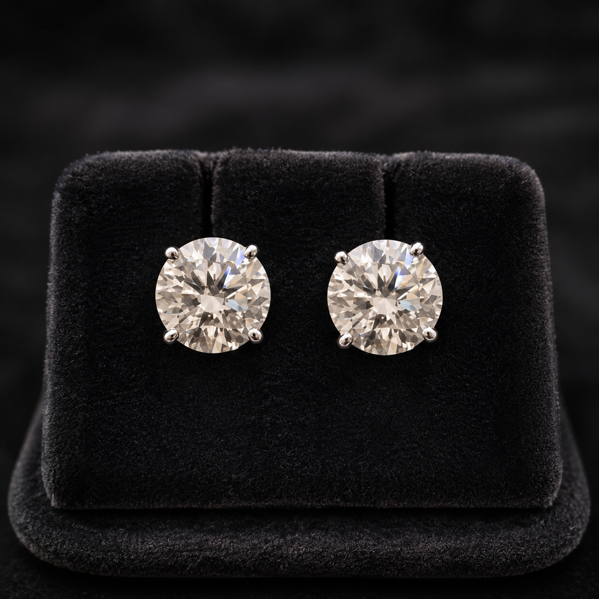 Round moissanite stud earrings in 925 silver with four-prong settings on black velvet display
