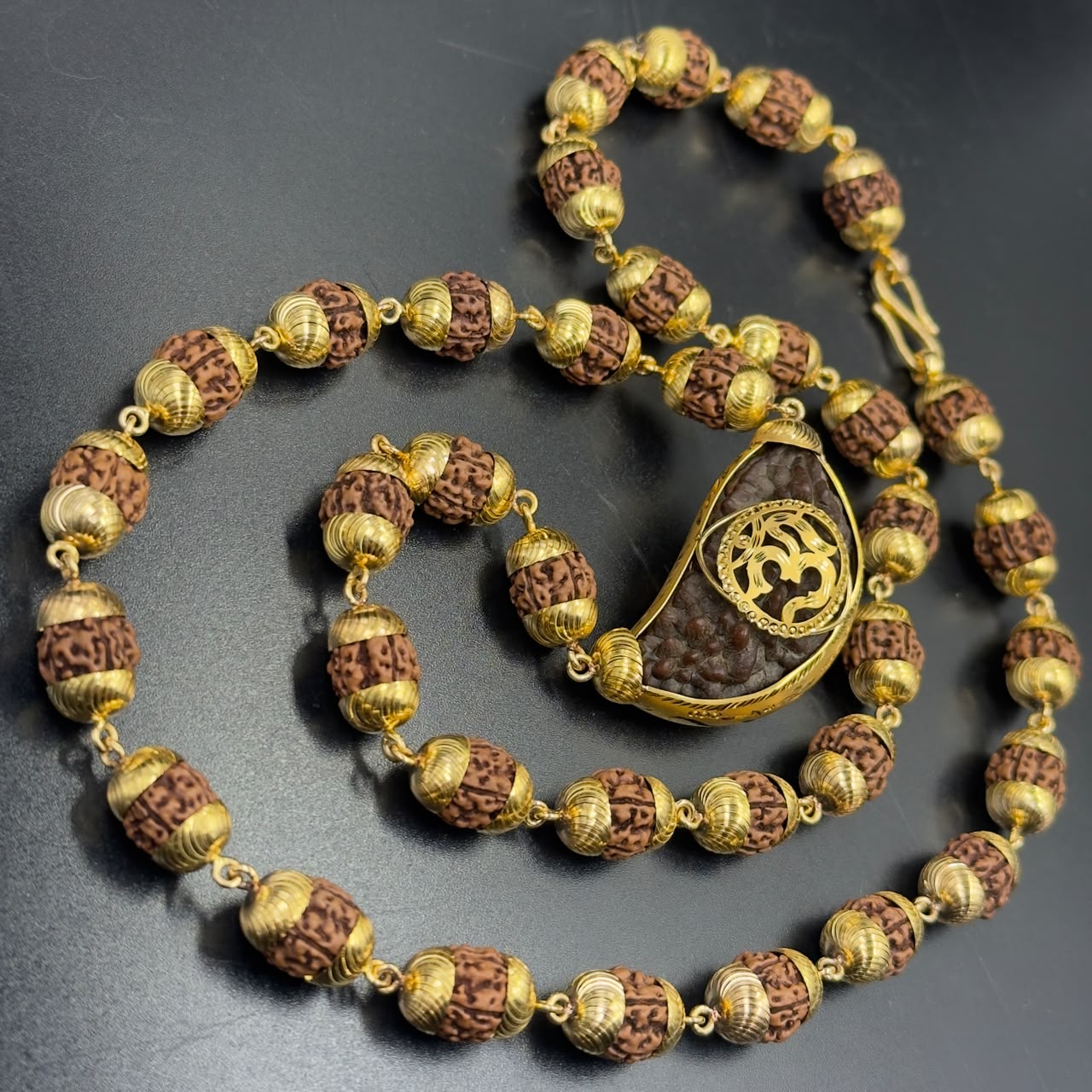 Rudraksha mala necklace with gold-toned beads and Om pendant on dark background