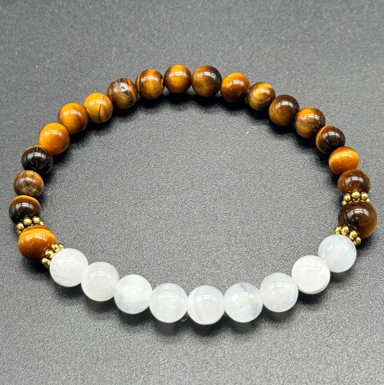 Close-up of selenite and tiger eye bead bracelet with gold accents on gray background