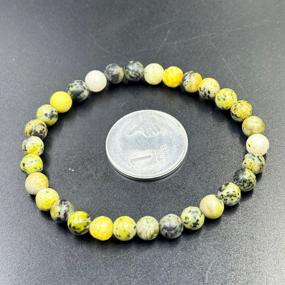 Close-up of serpentine beaded bracelet with mixed yellow and green stones and coin size