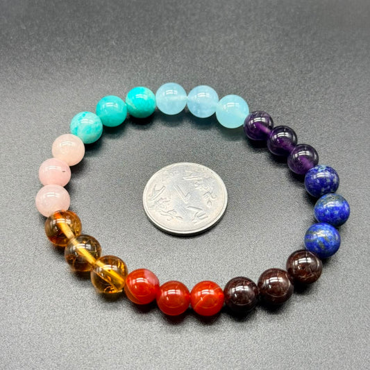 7 chakra balance bracelet with pastel blue, teal, and purple beads on gray fabric background