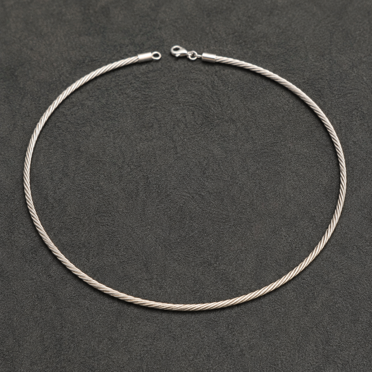 Silver Italian-style twisted hasli necklace with clasp and chain links laid on dark background