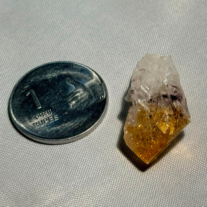 Single citrine rough pointer crystal with golden tip and clear body beside a penny