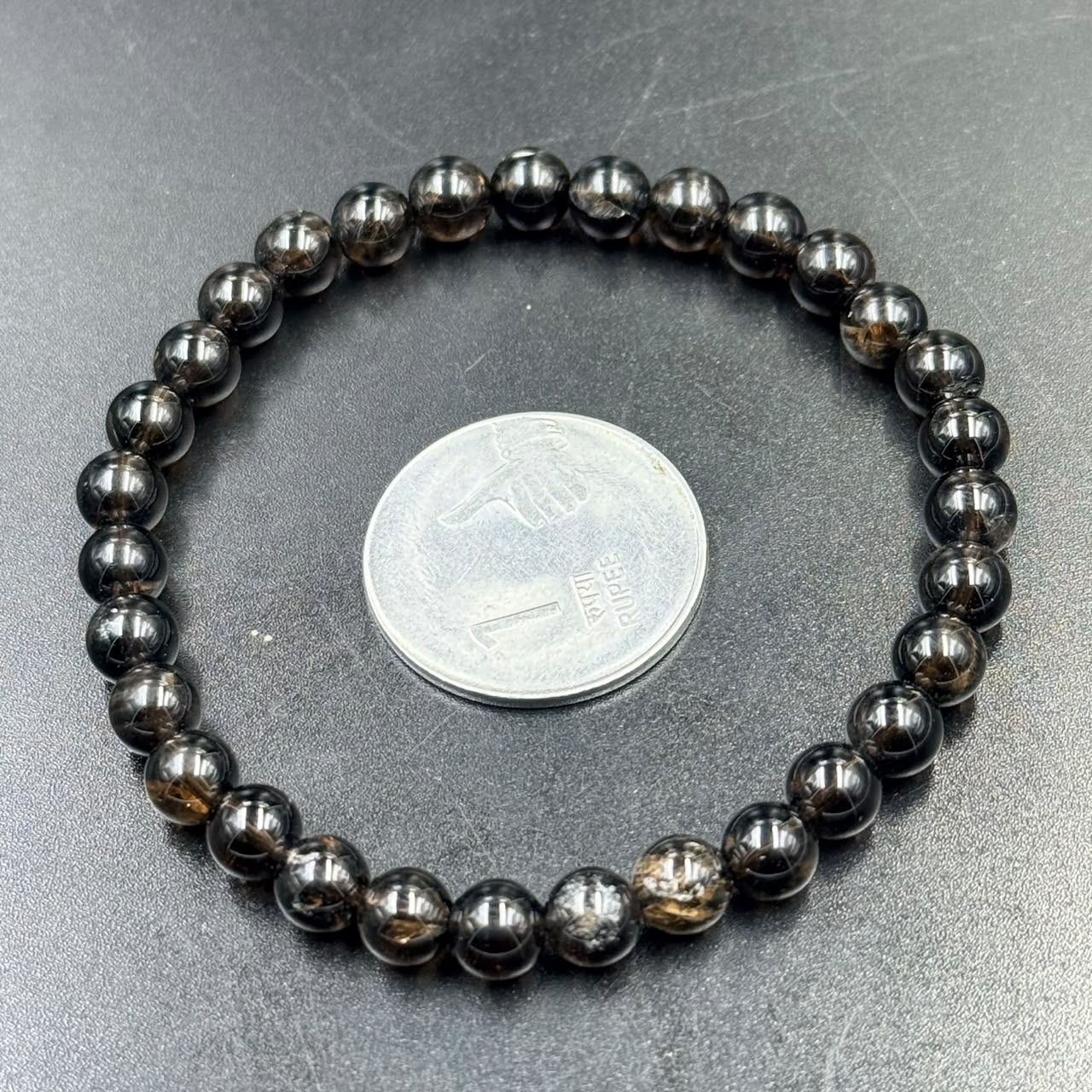 Smoky quartz bead bracelet close-up with round dark stones on gray textured background