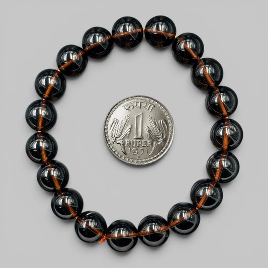 Smoky quartz bracelet looped on gray background with a coin for size comparison